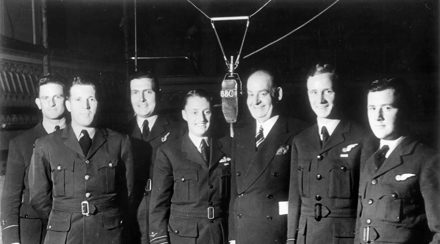 A group of seven Australians standing around a microphrone. Squadron Leader James Catanach is in the centre.