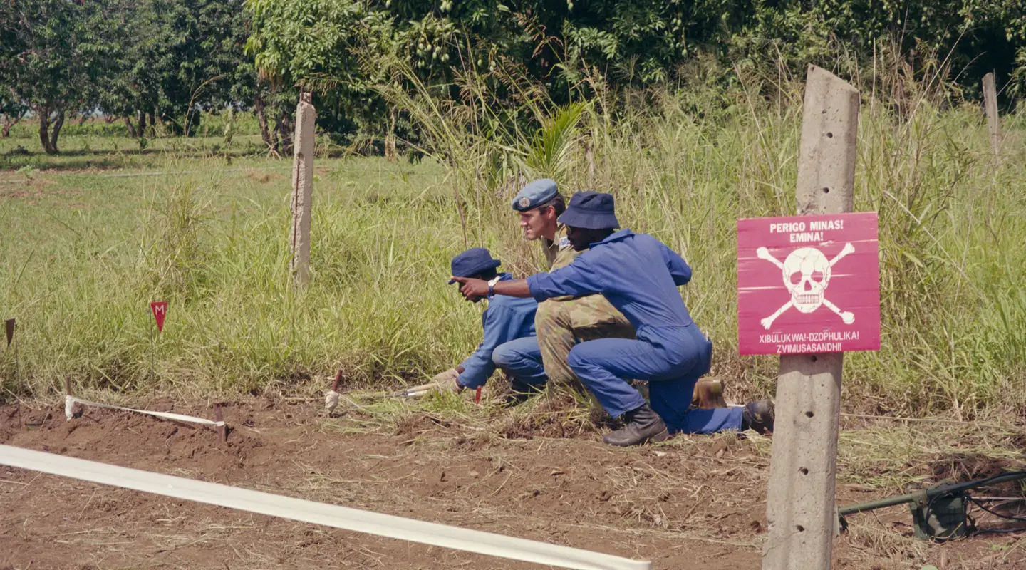 Major Peter Clay crouches in a field with two men.