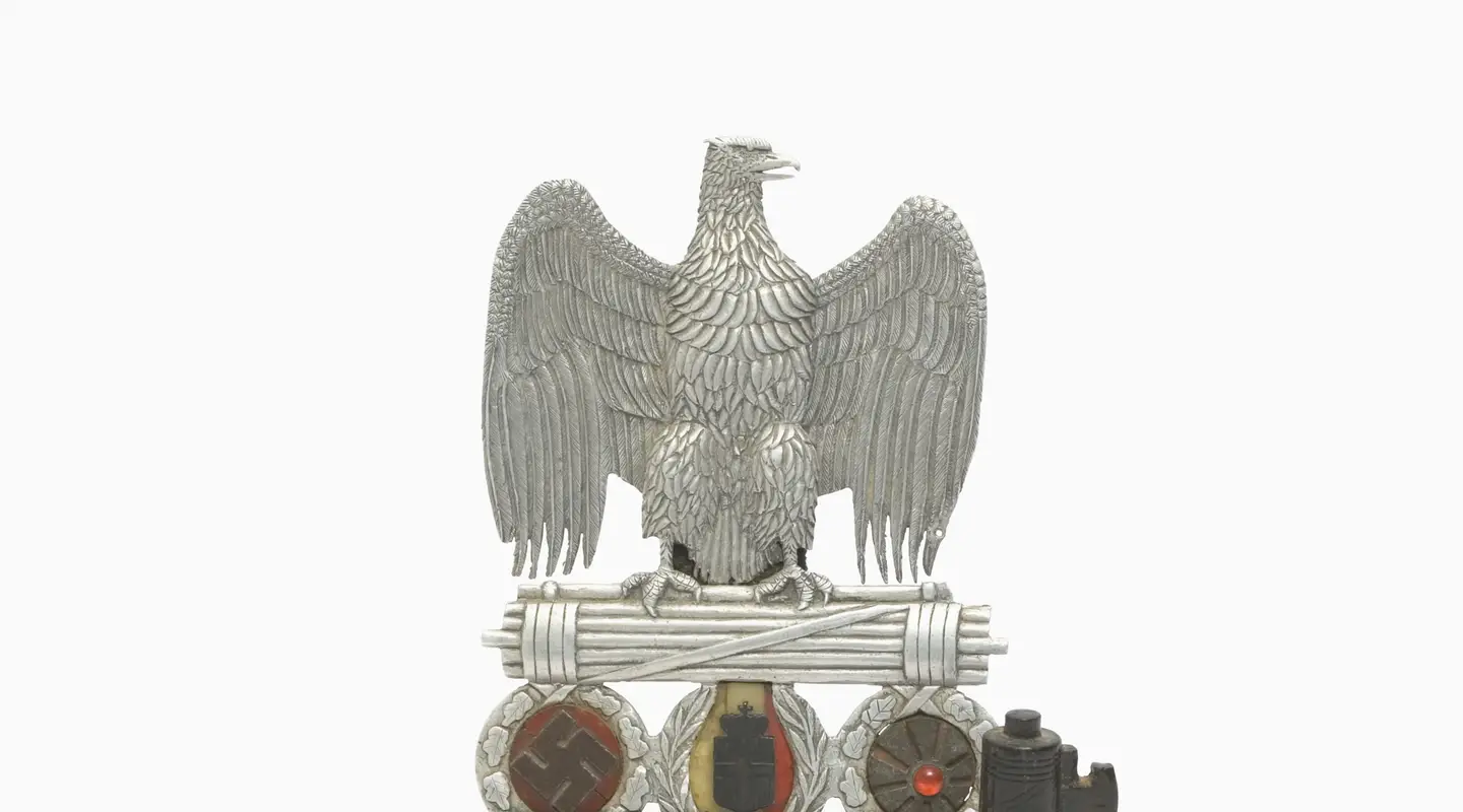  An ornate and fastidiously decorated fascist eagle clasping a Roman fasces, from which are suspended the symbols of the three Axis allies, each contained within a decorated wreath - from left to right, the Nazi swastika; the Italian arms and the Japanese 'rising sun' flag. 