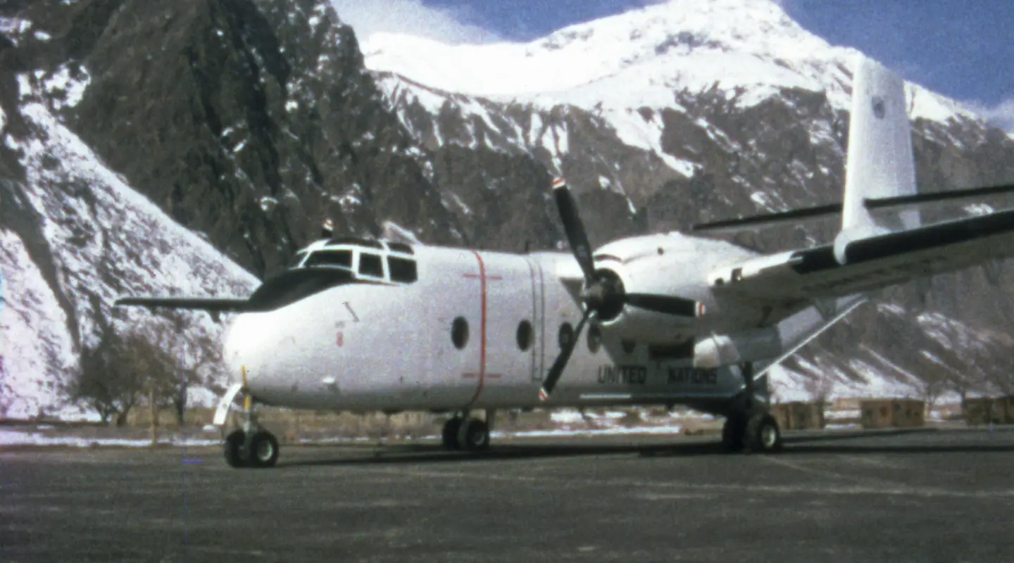 Front side view of a Caribou aircraft on an airstrip with snow capped mountains in the background