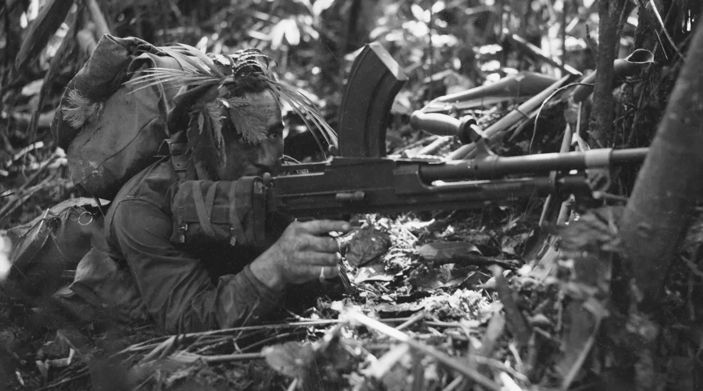 Australian soldier crouches on the ground with a Bren light machine gun