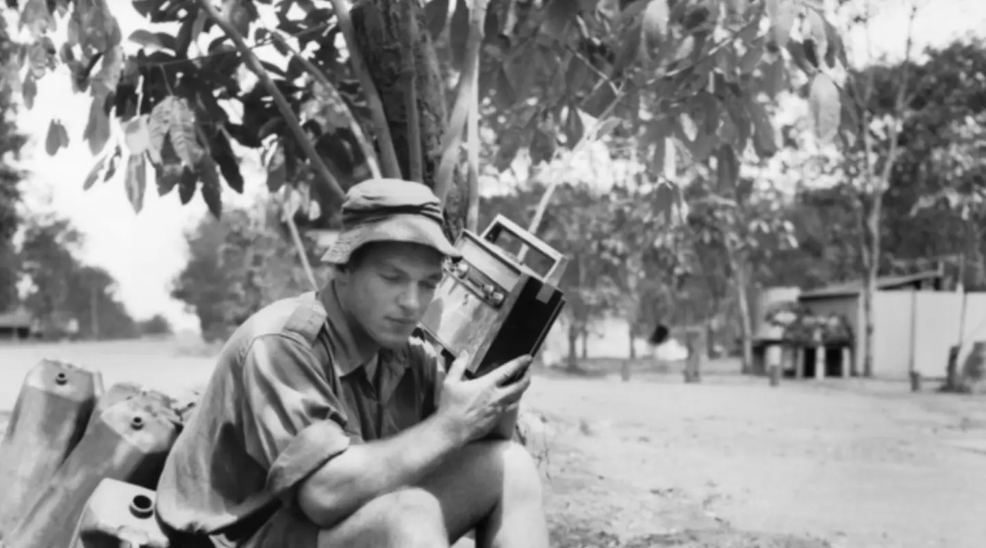 Holding a radio close to his ear as he listens to news from Australia is Private Robert Foot, 1RAR. 