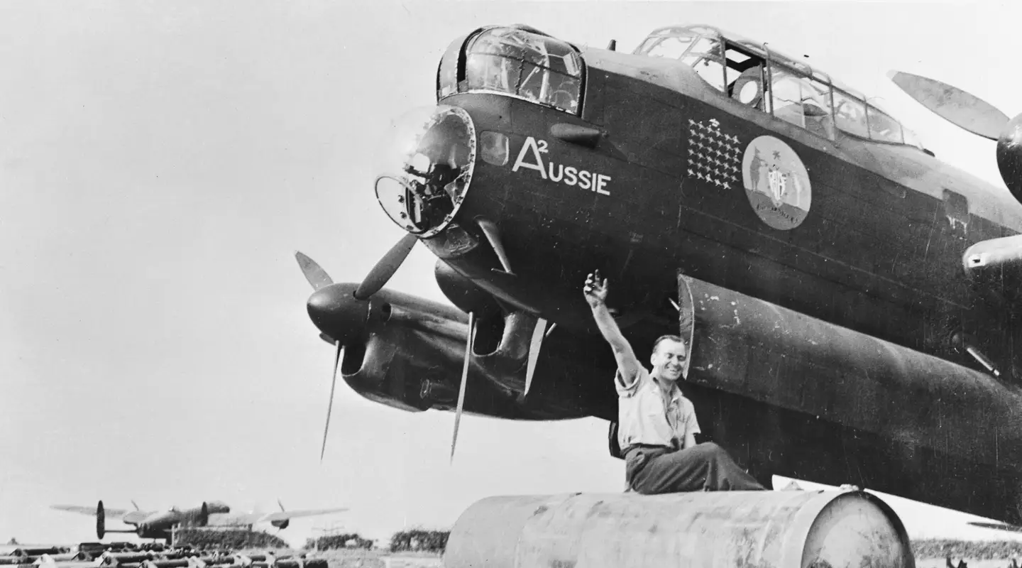 LINCOLNSHIRE, ENGLAND. 1943-09-09. CORPORAL W. E. DAWSON OF ALBERTON, SA, RIDING ON A "COOKIE" (4000LB BOMB) TO BE LOADED ONTO "A2" AUSSIE, A LANCASTER AIRCRAFT OF NO 460 SQUADRON RAAF BASED AT RAF STATION BINBROOK. THE NOSE ART ON THE AIRCRAFT IS THE AUSTRALIAN COAT OF ARMS. AWM UK0487