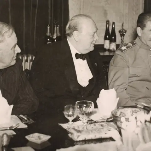 Three men in formal attire seated in a row at a dining table