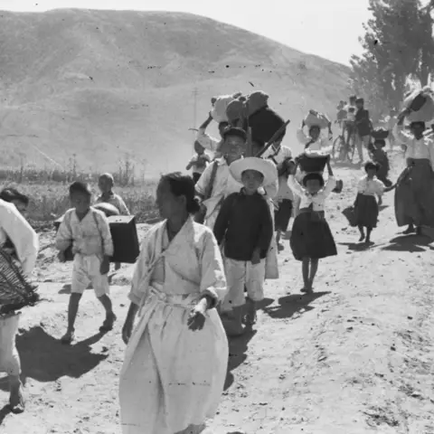 Korean refugees trudges along a dusty road away from the war.