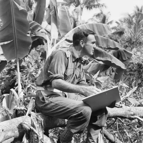 Captain Roy Hodgkinson, an official war artist, sits in dense jungle of New Guinea sketching.