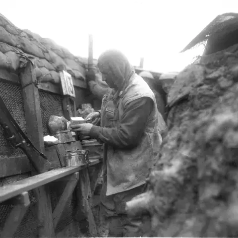 A member of the 39th Battalion cutting a piece of bread while in the front-line trenches.