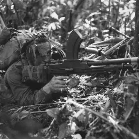 Australian soldier crouches on the ground with a Bren light machine gun