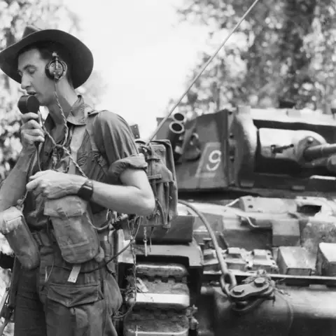 Australian soldier beside tank talks on the radio.