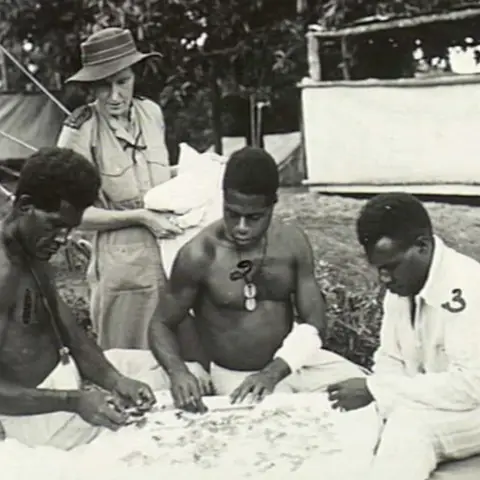 Three Papua New Guinean soldier do a puzzle, as a nurse looks 
