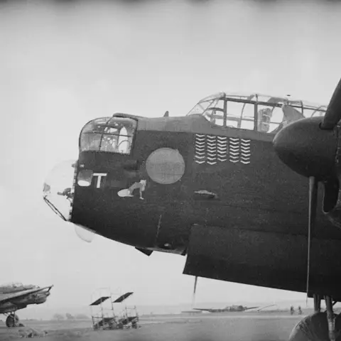 Nose art of 463 or 467 Squadron RAAF Lancaster bomber aircraft T-Tare. A reclining woman features in the artwork. The 37 operations flown by this aircraft are represented by boomerangs. This aircraft is fitted with a later style pitot tube, and rear view cupola over the bomb aimer's window (visible under the nose). AWM P02604.028