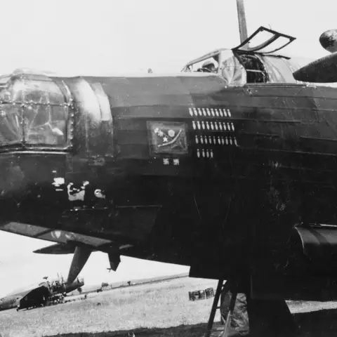 The forward fuselage of a Wellington Mark X bomber of No 142 Squadron RAF (LP 209 - J), The nose art is a piece of decorated aircraft fabric (Irish linen) which has been painted with a boomerang, a Welsh leek, a white Tudor rose, a white five pointed star of India and a green Canadian maple leaf on a white scroll. AWM P03978.001