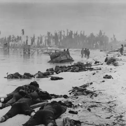 Bodies of dead US Marines, sprawled along the invasion beach on Tarawa Island near a crippled American tank