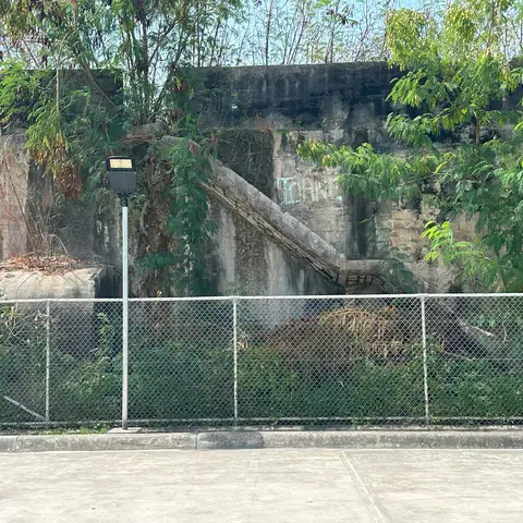 14.	Today the structure, bordered by a basketball court and church, is where UXO (unexploded ordnance) is stored. Photo credit Michael Garside.