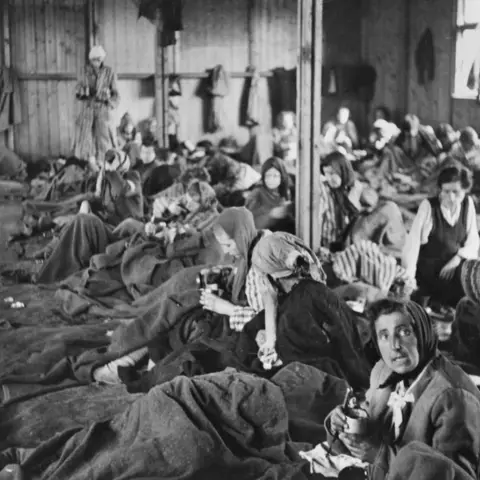 Female inmates of Belsen concentration camp sitting on the floor of a crowded hut.