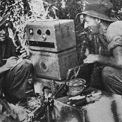 Sergeant Frank J Parmiter of Coburg, Vic, and Corporal Ivan G Pritchard, of Kensington, NSW, spotters with the New Guinea Air Warning Wireless Company (NGAWW), at work beside th