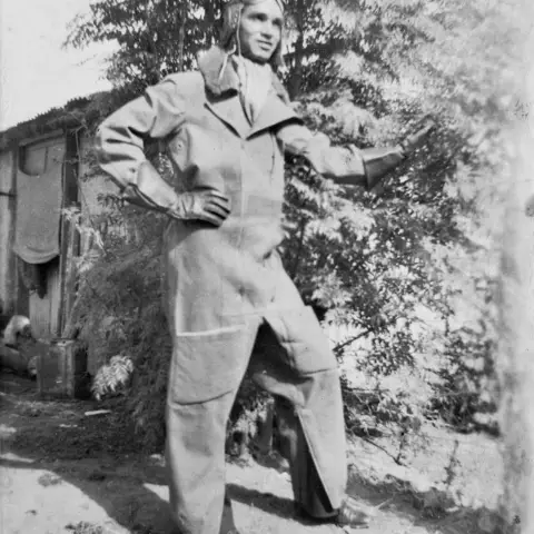 Man standing next to a tree where a polit's flying uniform 