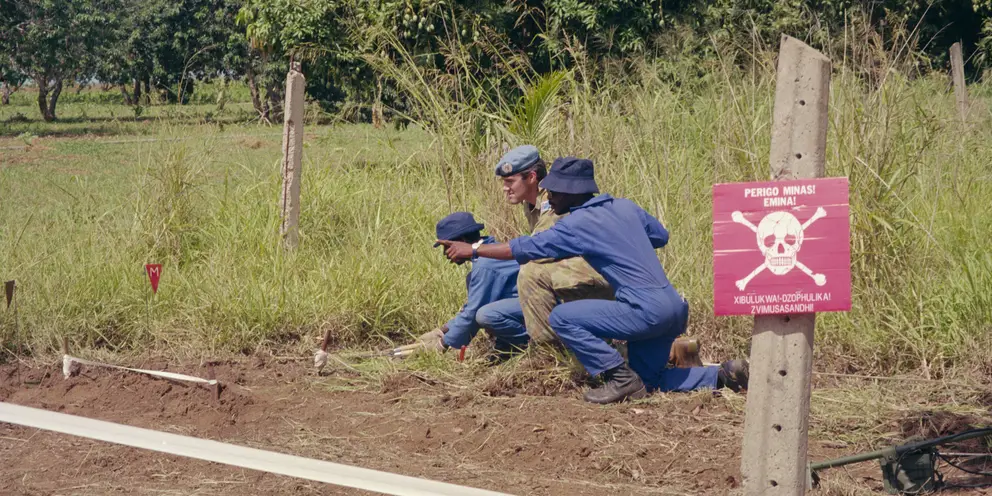 Major Peter Clay crouches in a field with two men.