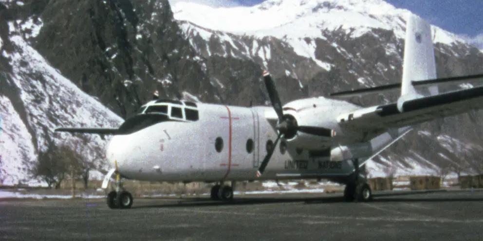 Front side view of a Caribou aircraft on an airstrip with snow capped mountains in the background