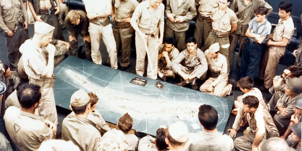 Marines and sailors study a relief model of Betio en route to Tarawa. Photo credit USMC 67706, US Naval History and Heritage Command 