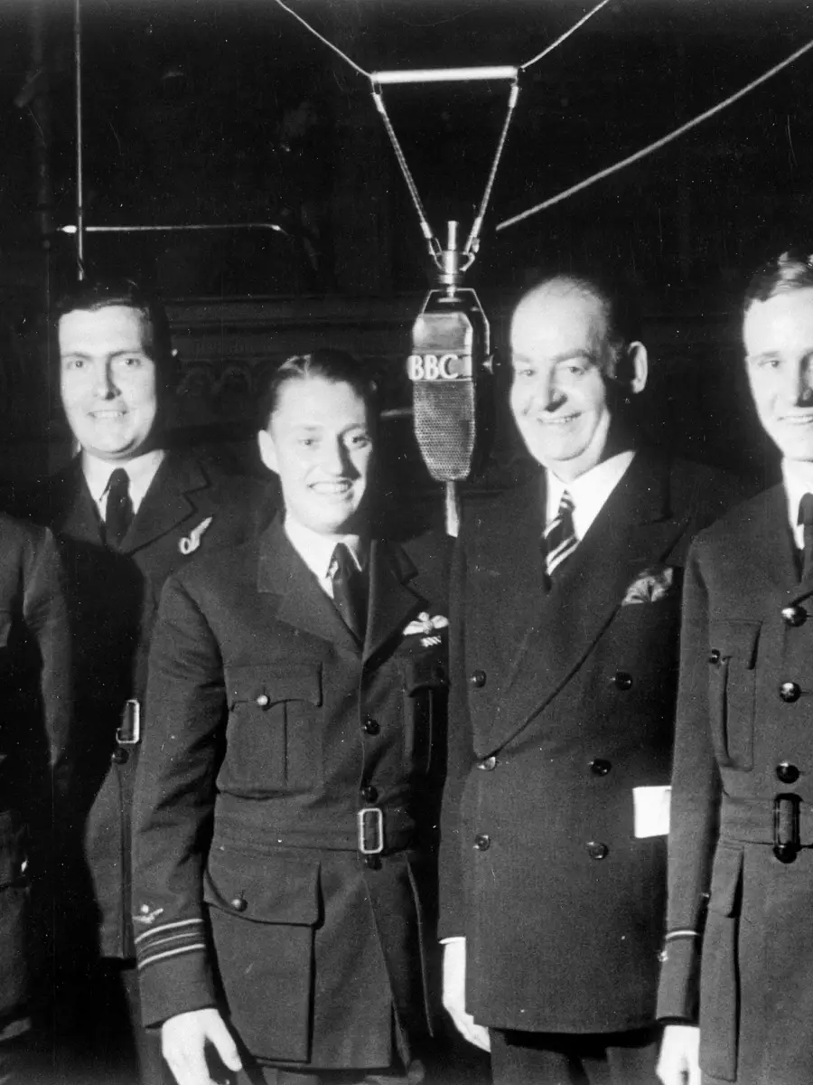 A group of seven Australians standing around a microphrone. Squadron Leader James Catanach is in the centre.