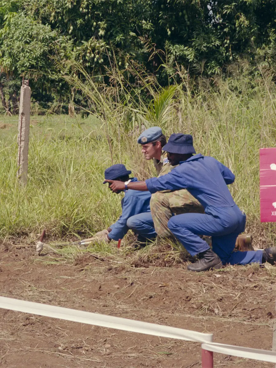 Major Peter Clay crouches in a field with two men.