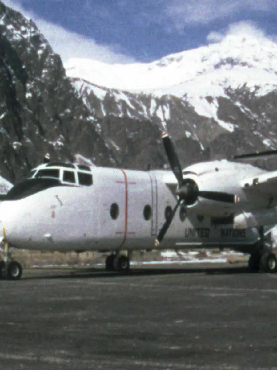 Front side view of a Caribou aircraft on an airstrip with snow capped mountains in the background