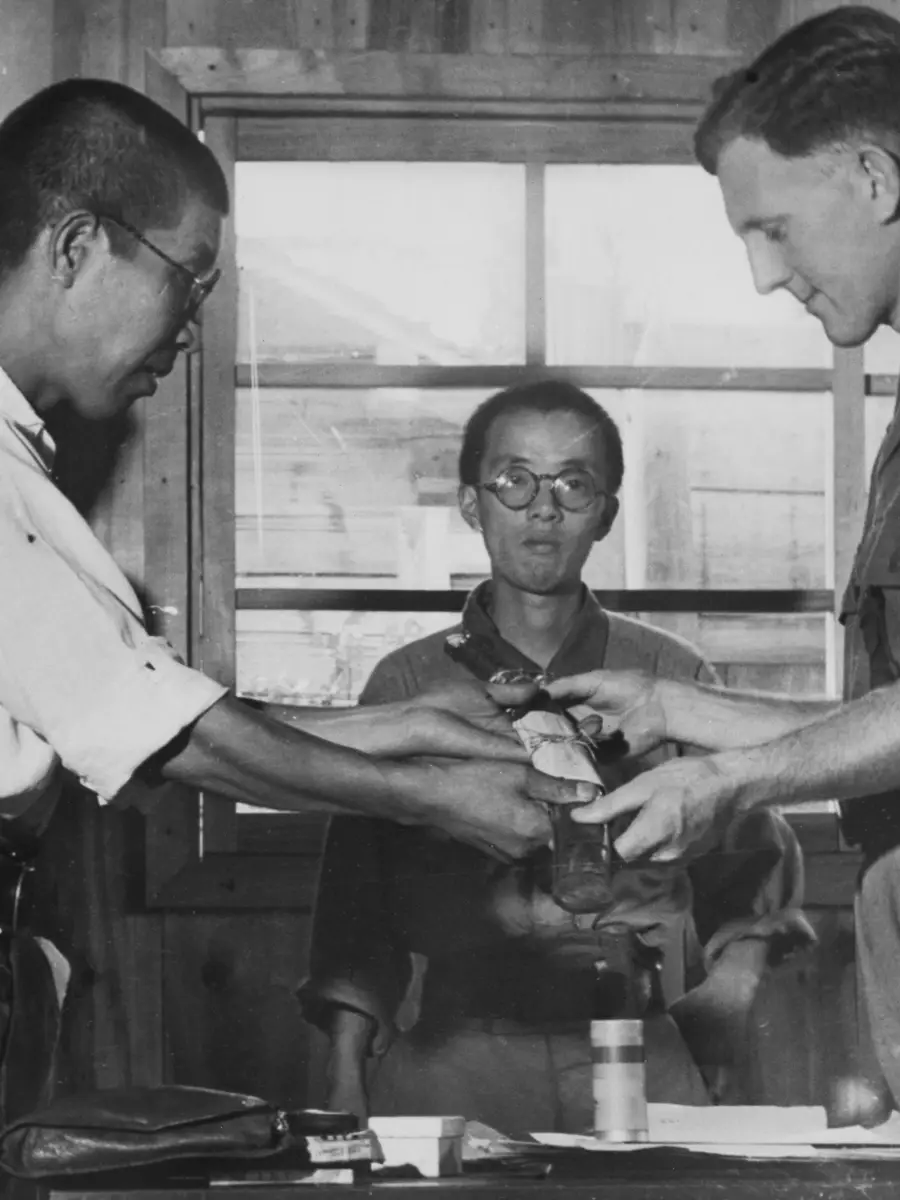 Second Lieutenant Nakanishi formerly Commandant of the Notogawa prisoner of war (POW) camp surrenders his sword (and command) to Lt Goddard who was captured at Singapore on 15 February 1942