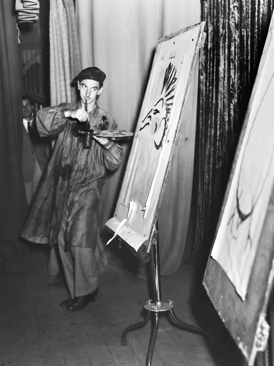 Norman Hetherington in his stage costume and two easels doing a painting