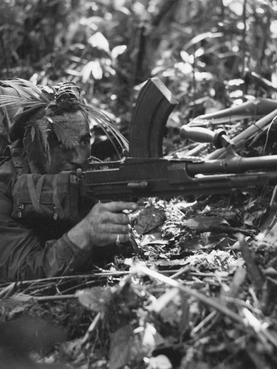 Australian soldier crouches on the ground with a Bren light machine gun