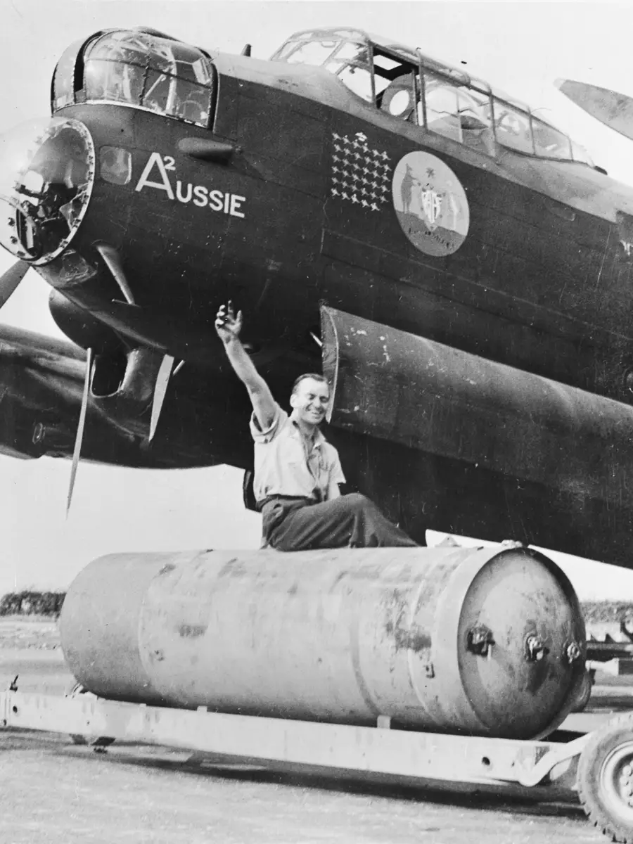 LINCOLNSHIRE, ENGLAND. 1943-09-09. CORPORAL W. E. DAWSON OF ALBERTON, SA, RIDING ON A "COOKIE" (4000LB BOMB) TO BE LOADED ONTO "A2" AUSSIE, A LANCASTER AIRCRAFT OF NO 460 SQUADRON RAAF BASED AT RAF STATION BINBROOK. THE NOSE ART ON THE AIRCRAFT IS THE AUSTRALIAN COAT OF ARMS. AWM UK0487