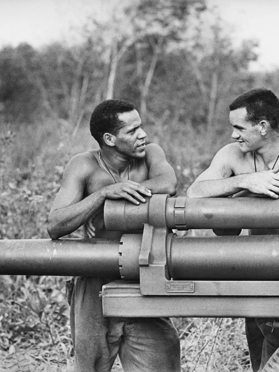 Two men standing, facing each other, arms resting on artillery cannon