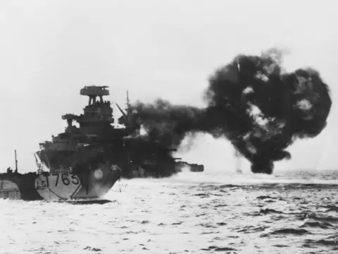 A Landing Craft Tank heads to shore as a US battleship bombards the shore