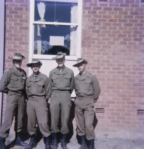 Group portrait or four National Servicemen recruits and room-mates in front of the new three-storied brick accommodation blocks at Kapooka in which they lived while undergoing basic training.