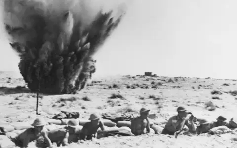  Mortar bombs explode behind a slit trench occupied by Australian troops of the 9th Division at Ruin Ridge, September 1942. AWM 151150 