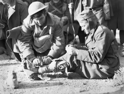  An Italian prisoner captured near Bardia receives medical treatment from an Australian soldier of the 2/1 st Battalion in January 1941. AWM 004914