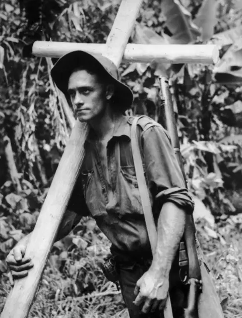 Private James Oliver, 31/51st Battalion, carries a cross to mark the grave of a fallen comrade, Bougainville, 1945
