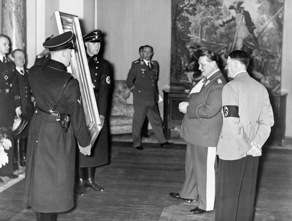 Adolf Hitler presents to Hermann Goring a painting that two SS men hold.