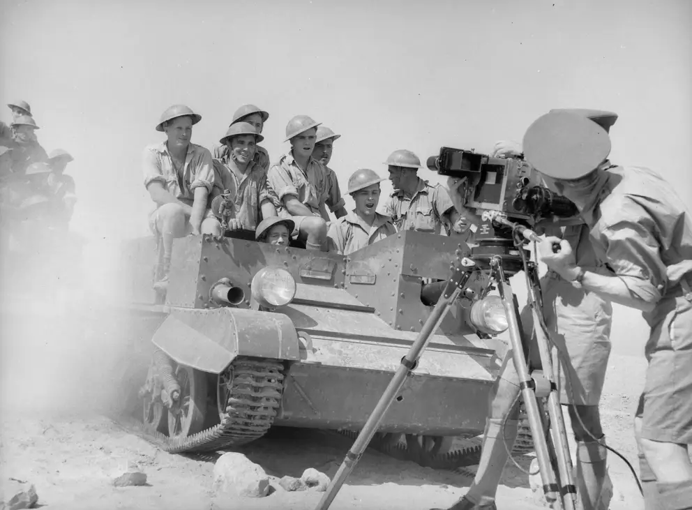 Frank Hurley and Damien Parer film Australian troops as they ride past in a carrier.