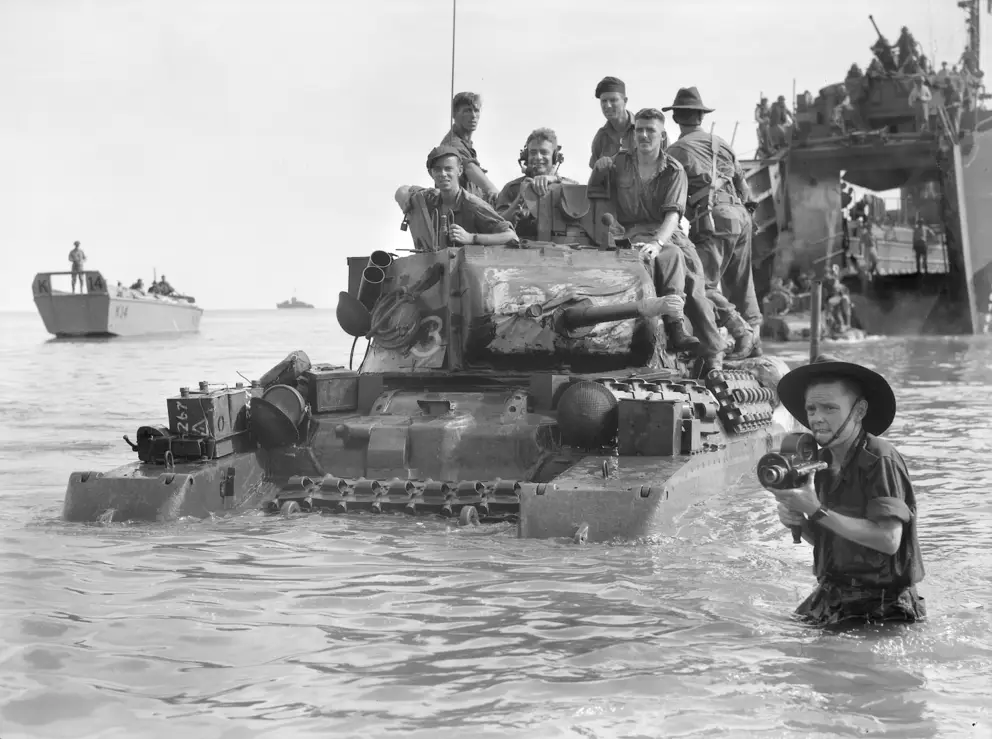 Corporal Douglas Charles Hardy wades ashore carrying a Bell & Howell cine camera as Matilda tanks of 2/9th Armoured Regiment disembark